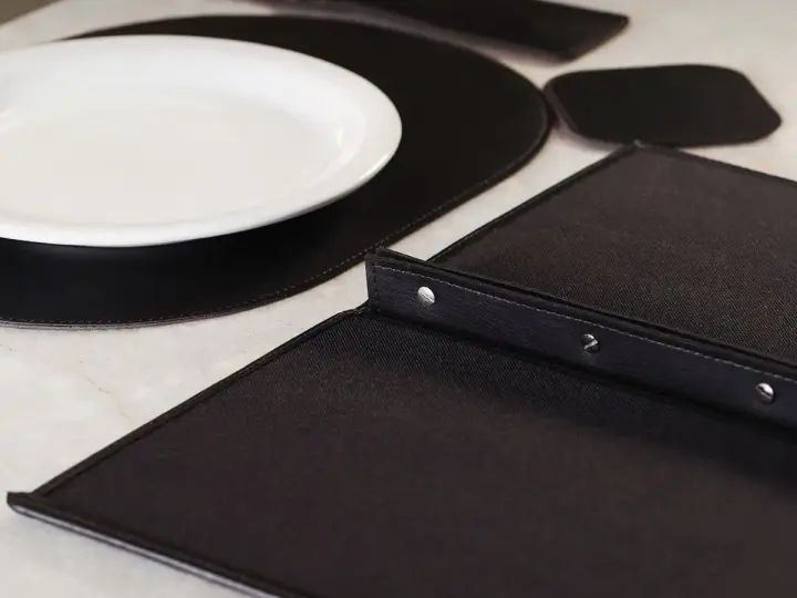 Sousplat de couro sob o prato, com porta-copo e cardápio na mesa